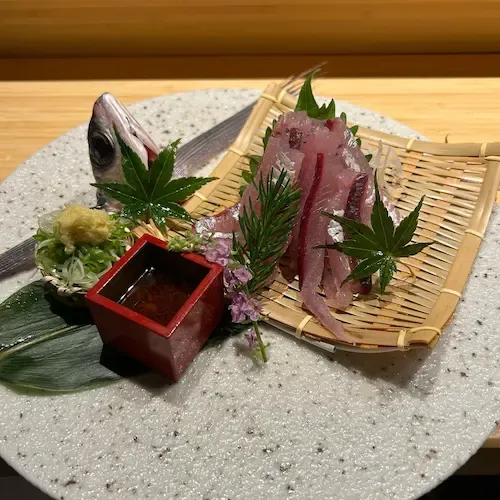 Sashimi with dipping sauce, decorated with fish head and greens